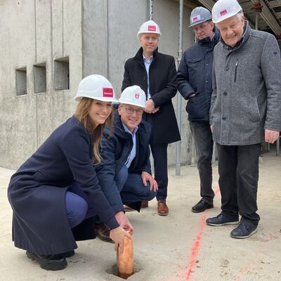 F&uuml;nf Personen stehen auf der Baustelle um ein kleines Loch, in das zwei Personen ein Kupferrohr versenken.