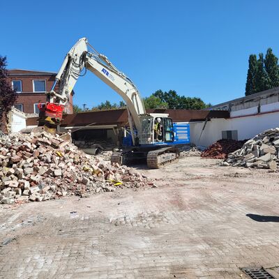 Ein Bagger bei Abrissarbeiten auf einer gepflasterten Fl&auml;che.