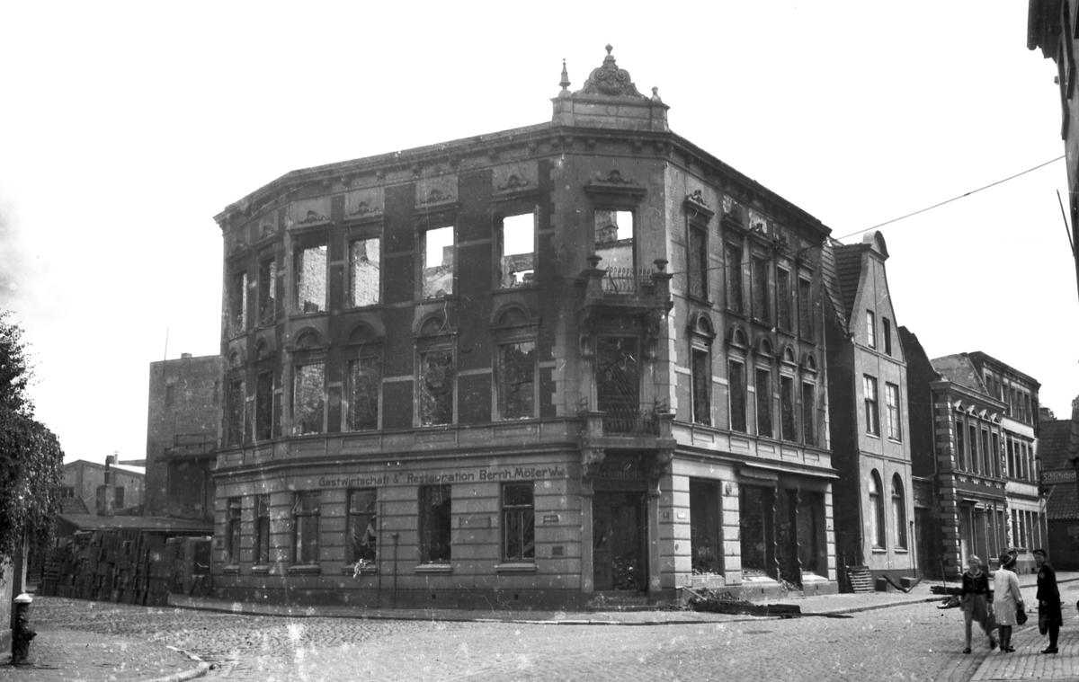 Bild vergrößern: Ein im zweiten Weltkrieg ausgebombtes mehrgeschossiges Wohnhaus steht an einer Straßenkreuzung. Die Fenster sind leer, von dem Gebäude steht nur noch die Fassade.